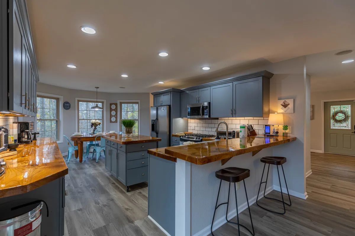 The kitchen island with bar stools is the focal point, surrounded by appliances and large windows. The layout encourages socializing, cooking, and sharing meals, and the welcoming ambiance enhances the sense of shared experience.
