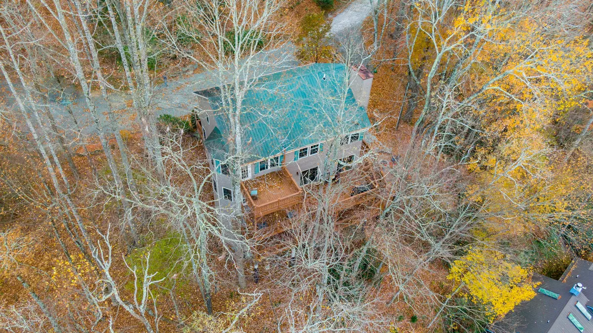 This image highlights the home's deck nestled within a wooded landscape, with tall trees enveloping the area. The peaceful setting encourages bird watching, nature walks, or simply unwinding outdoors while enjoying the sights and sounds of the forest.
