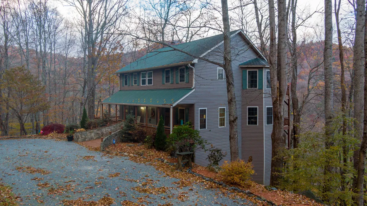 This exterior image showcases the home nestled among mature trees, with a broad driveway leading up to the house and a welcoming porch. The surrounding natural landscape hints at the seasonal beauty that can be enjoyed throughout the year.