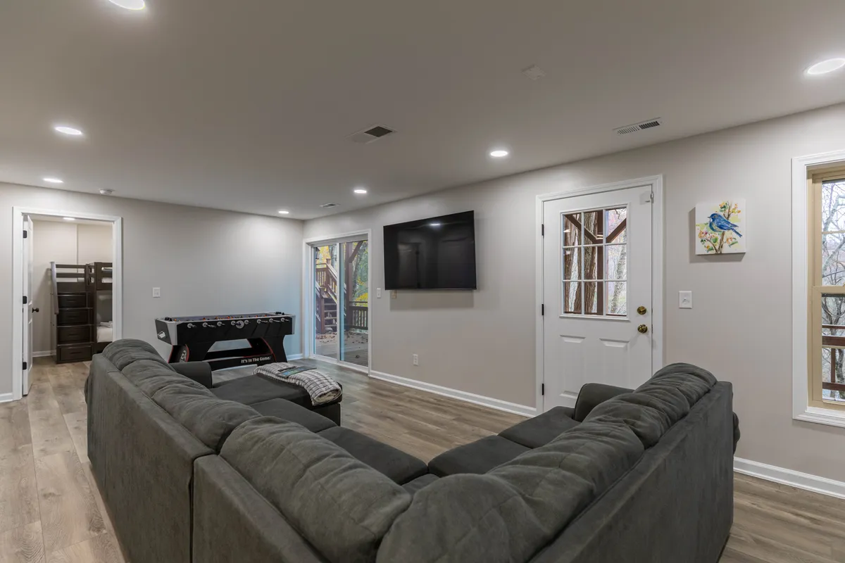 This image showcases a sofa facing a television, with a game table nearby and easy access to the outdoors. The setup is ideal for board games, streaming marathons, or simply relaxing. The connection to the outside hints at the room's versatility, including options for both play and rest.