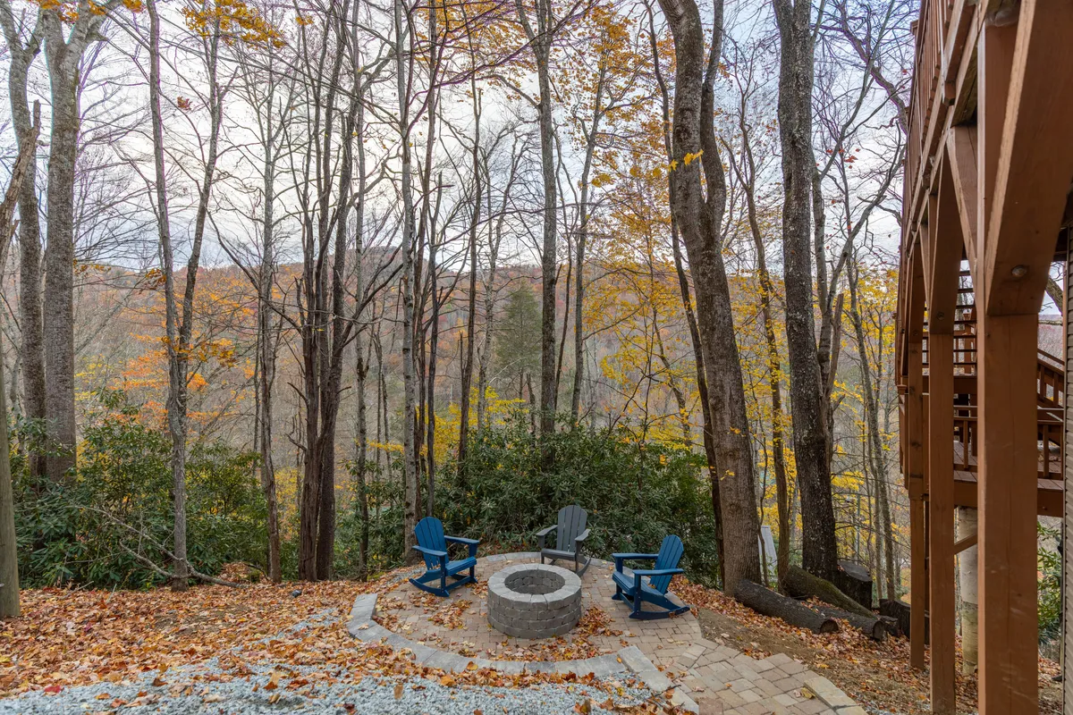 A fire pit encircled by comfortable chairs set amidst a grove of trees with vibrant autumn leaves, creating a cozy and inviting outdoor gathering spot. The scene is ideal for groups to enjoy stories, s’mores, and the peacefulness of nature.