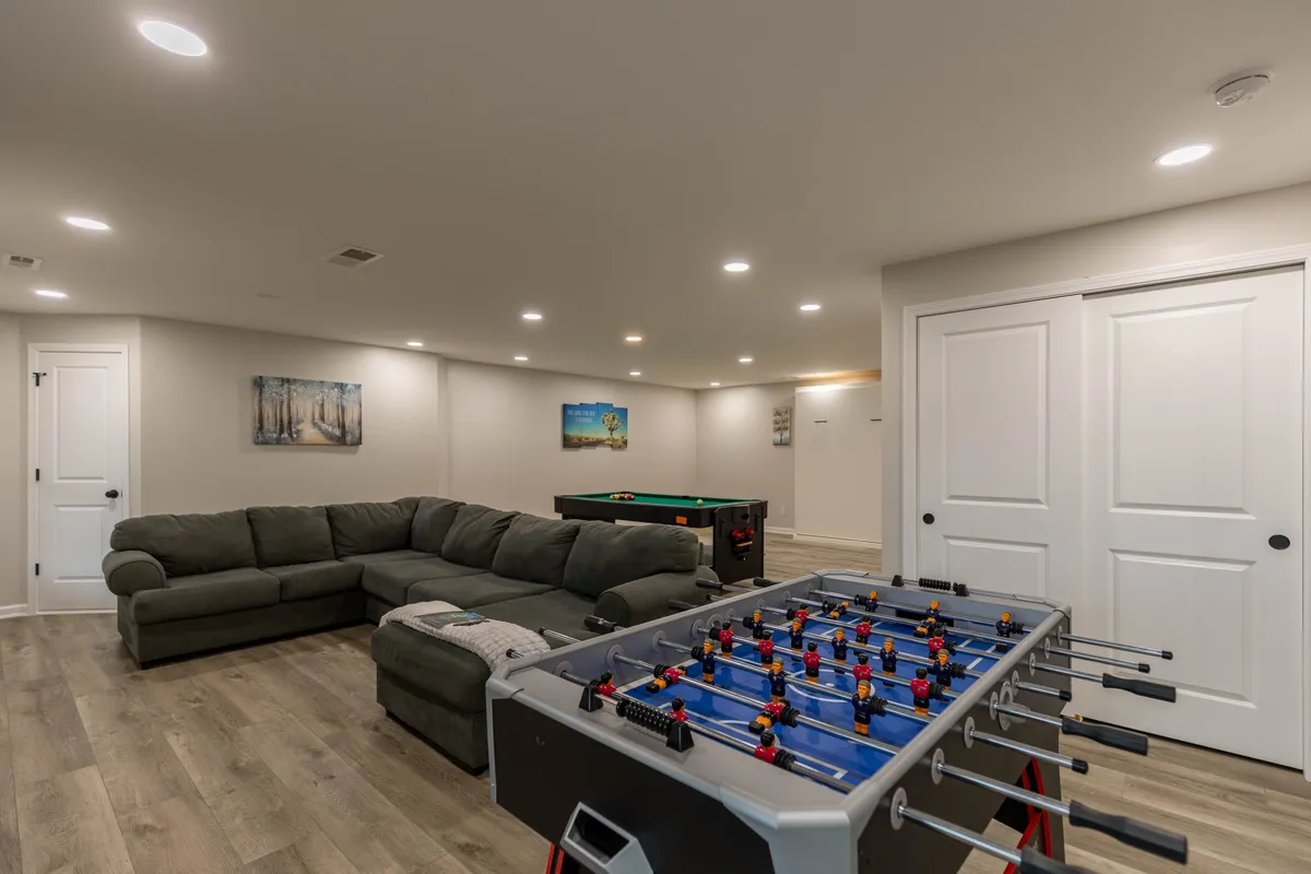 This image features the heart of the game room: a foosball table, a sectional sofa, and a pool table. The arrangement clearly invites social interaction and friendly competition, while the bright and playful atmosphere is perfect for group gatherings. The spacious sectional is ideal for board games or movie nights, and the variety of entertainment options is on full display.
