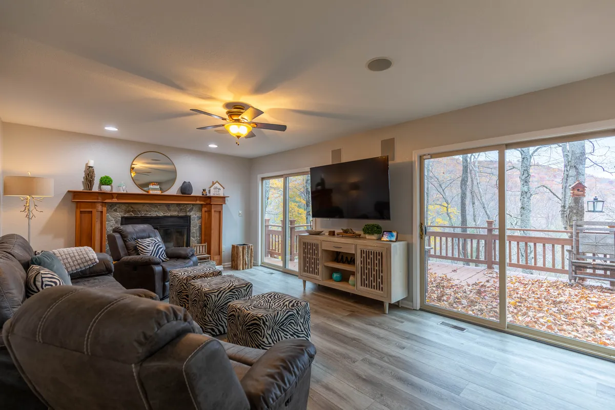 This image showcases the main living area featuring a large woodburning fireplace, comfortable seating, a TV, and expansive windows that let in natural light. The warm, inviting décor sets a cozy atmosphere ideal for group gatherings, relaxation, and movie nights.