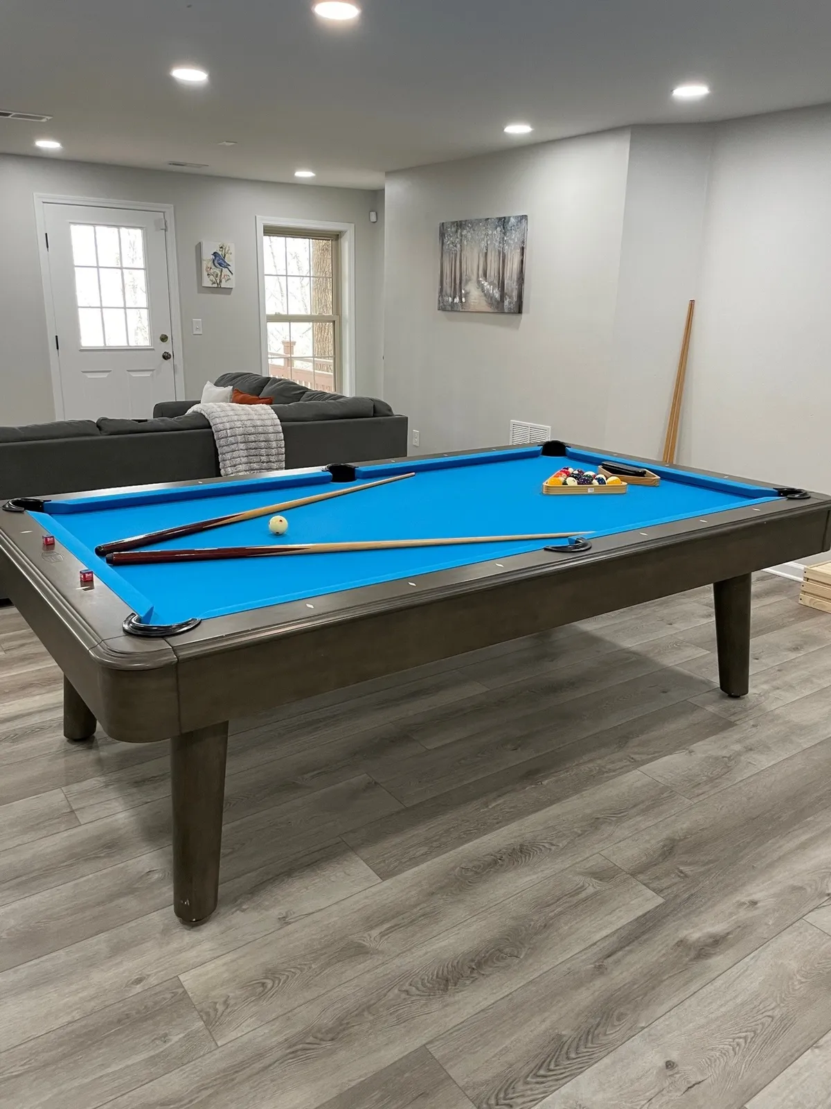 A closer look at the pool table and a comfortable sofa, with vibrant wall art adding personality and color. The setup is perfect for both competitive pool matches and relaxed hangouts, echoing the room’s multi-functional design. The casual, friendly mood supports the idea of multi-generational bonding and group fun.
