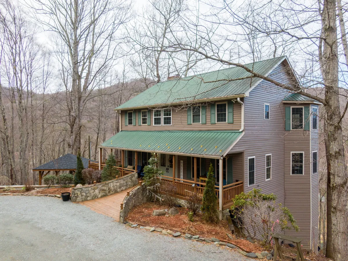 This image showcases the exterior of the home nestled among mature trees, with a welcoming front porch and a stone pathway leading up to the entrance. The scene is tranquil, emphasizing the secluded, natural environment that surrounds Peaceful Wood Haven.